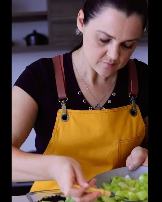 Elisabete cortando legumes, de avental amarelo