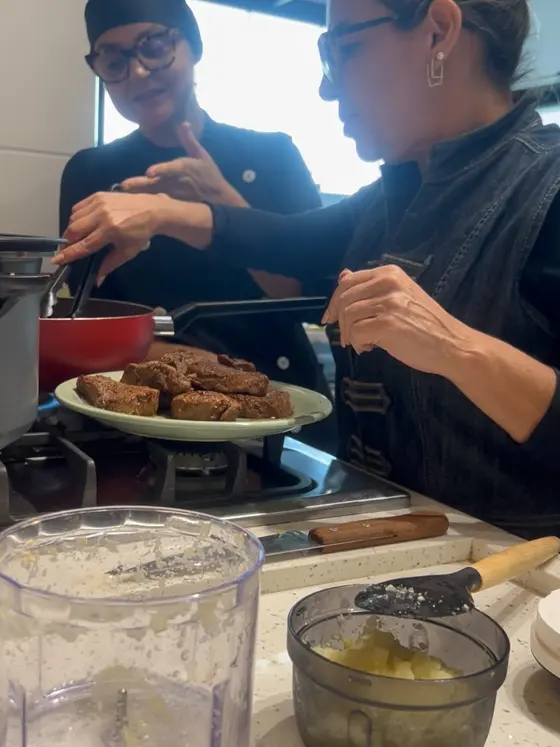 Elisabete e uma aluna lado a lado no fogão, provando o preparo