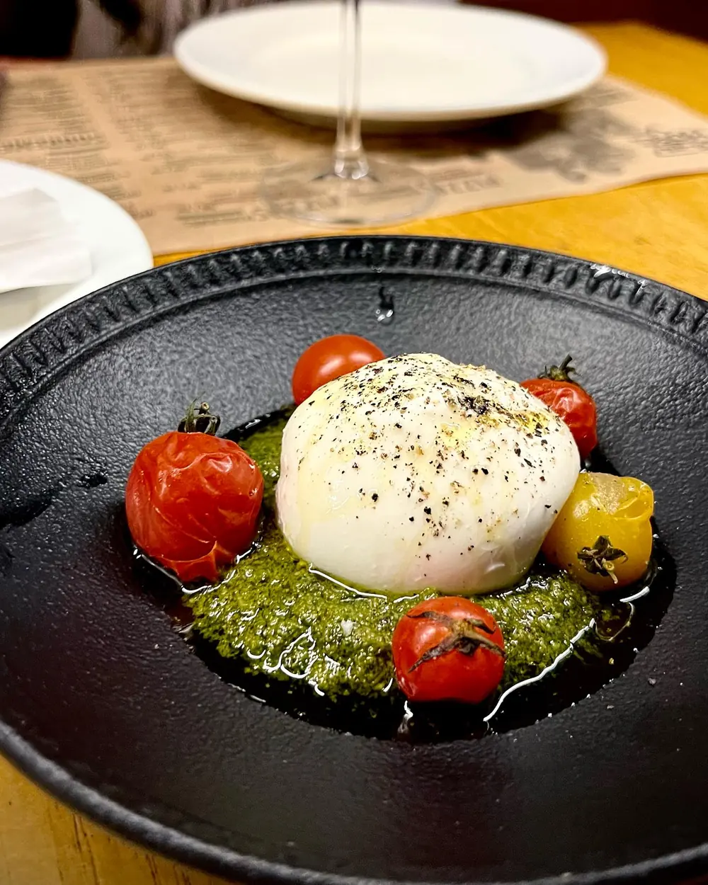 Burrata ao pesto com tomatinhos servida em prato preto